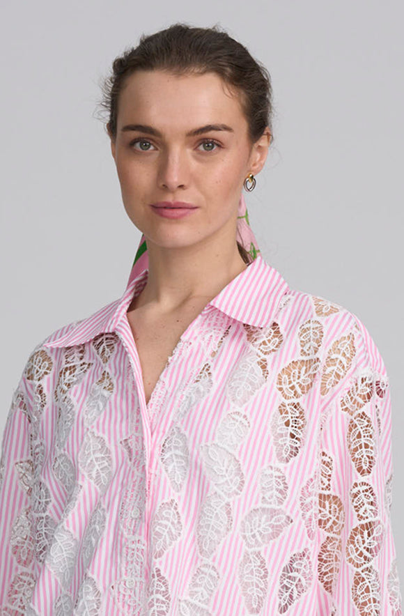 A woman wearing a pink and white striped button-down shirt with white floral lace overlays, photographed against a solid gray background.